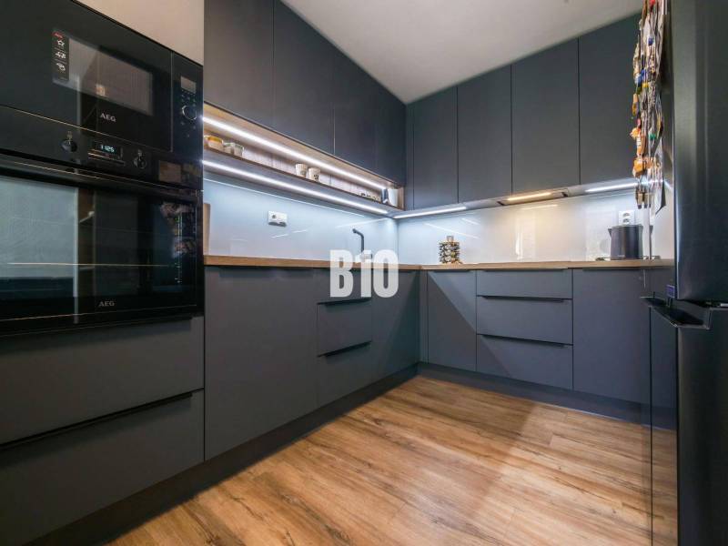 Konyha egy háromszobás lakásban sötét szekrényekkel és fa dekorációjú padlóval.