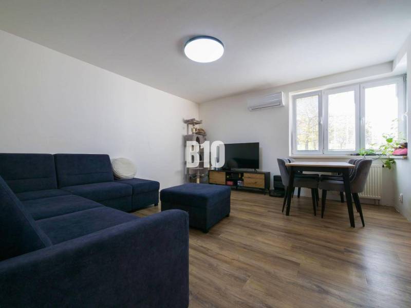 Nappali egy háromszobás lakásban kanapéval, televízióval és fa dekorációjú padlóval.