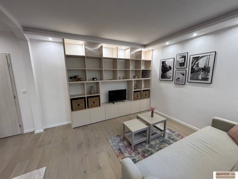 Nappali egy kétszobás lakásban kanapéval, polccal és fa dekorációjú padlóval.