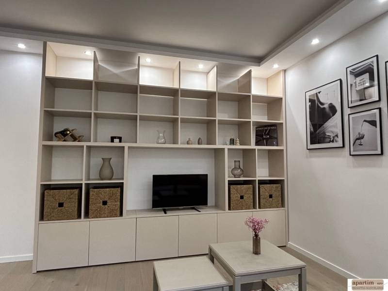 Tárolófal polcokkal és dekorációkkal egy kétszobás lakásban, mellette egy asztal virágokkal.