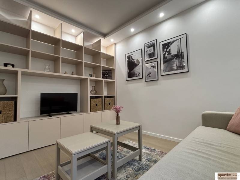 Nappali egy kétszobás lakásban beépített polcos fallal, dekorációkkal és kanapéval.