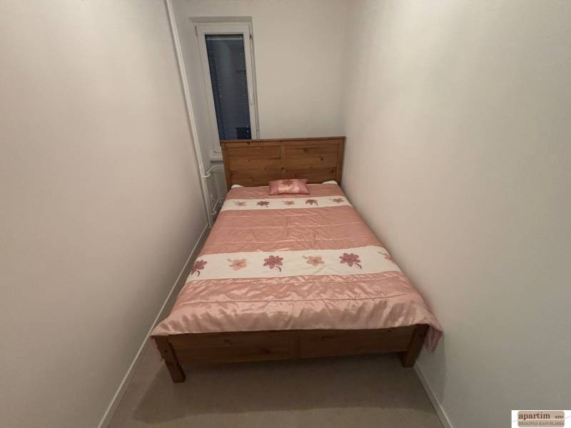 Keskeny hálószoba egy kétszobás lakásban, fa ággyal és virágos takaróval.