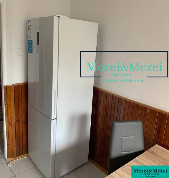 Konyha egy kétszobás lakásban, hűtőszekrény, fa burkolat, szürke szék, étkezőasztal.