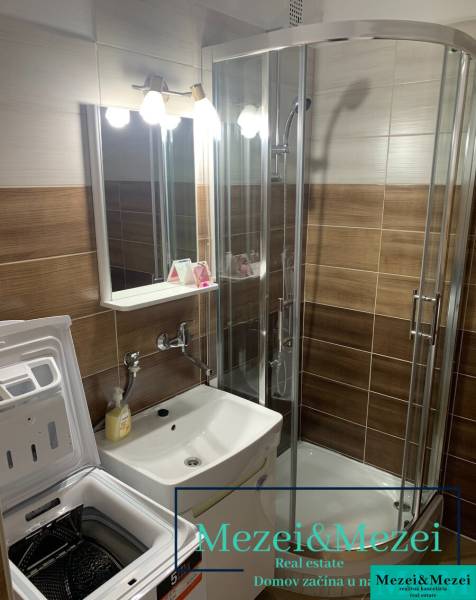 Fürdőszoba mosdóval, mosógéppel és zuhanyzóval egy kétszobás lakásban.