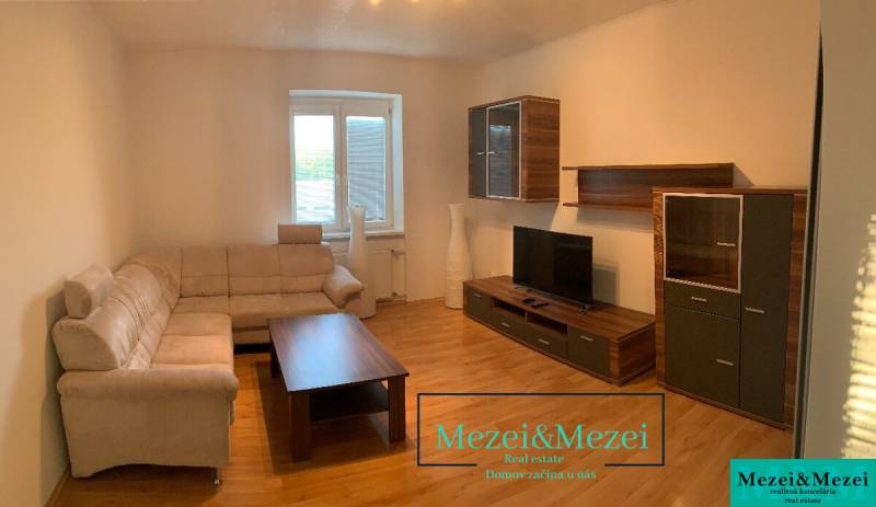 Nappali bézs kanapéval, fa bútorokkal és fa dekorációjú padlóval.