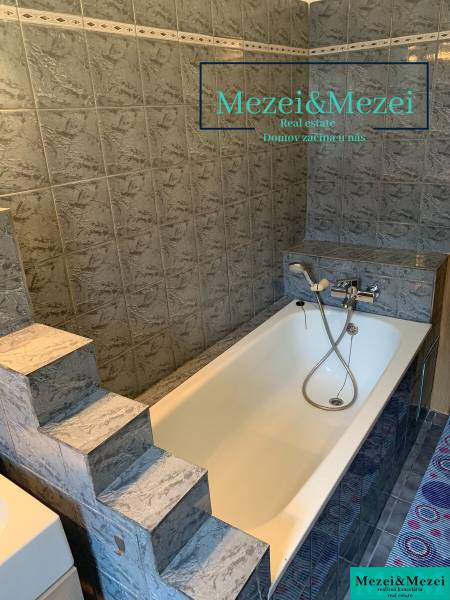 Fürdőszoba lépcsőkkel és káddal, szürke csempékkel körülvéve egy kétszobás lakásban.