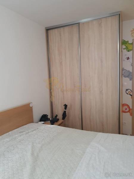 Hálószoba egy kétszobás lakásban, tolóajtós szekrény, ágy takaróval és éjjeliszekrény.