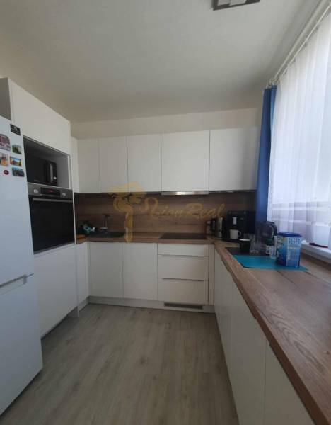 Konyha fehér szekrényekkel, fa dekorációval a padlón és munkalapon egy kétszobás lakásban.