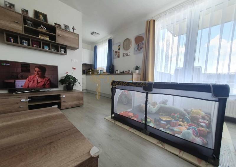 Világos nappali szoba fa mintázatú padlóval és játékokkal teli járóka egy kétszobás lakásban.