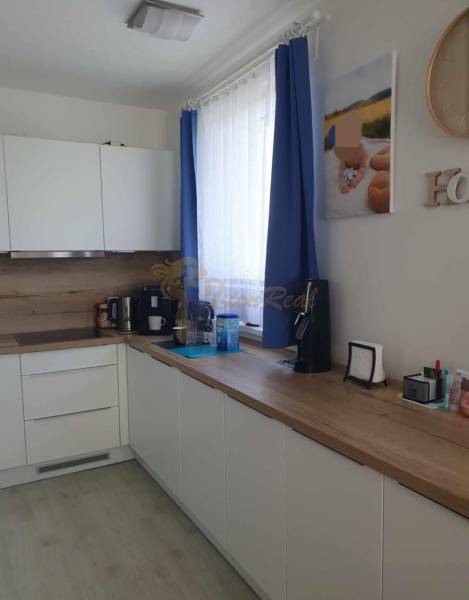 Konyha egy kétszobás lakásban fehér szekrényekkel és fa mintázatú padlóval.