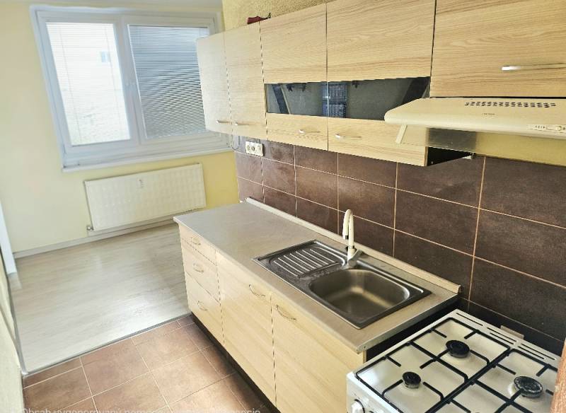 Konyha egy kétszobás lakásban fehér szekrényekkel és fa mintázatú padlóval.