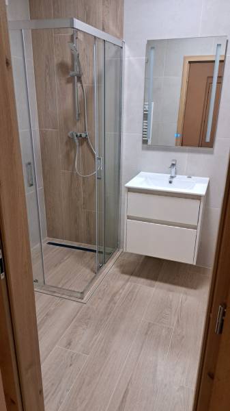 Fürdőszoba fa mintázatú padlóval, zuhanyzóval és mosdóval egy kétszobás lakásban.