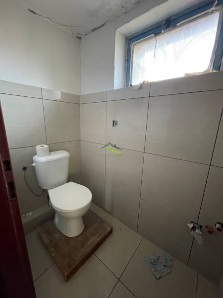 WC családi házban ablakkal és világos csempékkel a falakon.