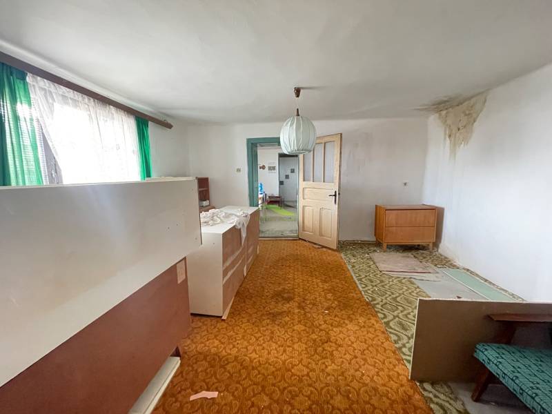 Családi ház belső tere szőnyeggel, régi bútorokkal és zöld függönyökkel az ablakon.