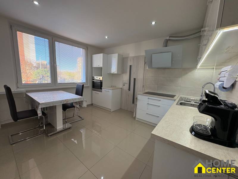 A háromszobás lakás konyhája nagy ablakokkal, étkezőasztallal és világos padlóval.