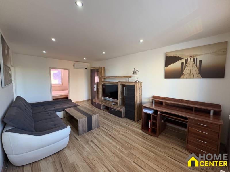 Nappali egy háromszobás lakásban, fa mintázatú padlóval és kényelmes ülőgarnitúrával.