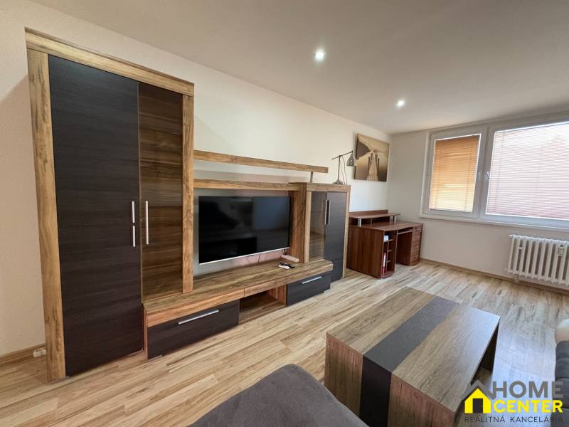 Nappali egy háromszobás lakásban, fa mintázatú padlóval és modern bútorokkal.