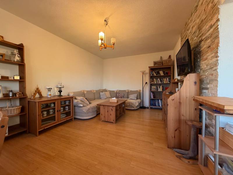 Nappali kanapéval, fa dekoros padlóval, könyvtárral és falra szerelt televízióval.