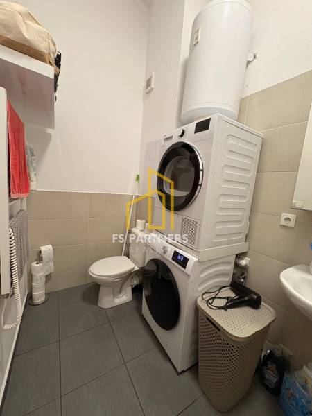 Fürdőszoba egy kétszobás lakásban mosógéppel, szárítógéppel, WC-vel és mosdóval.