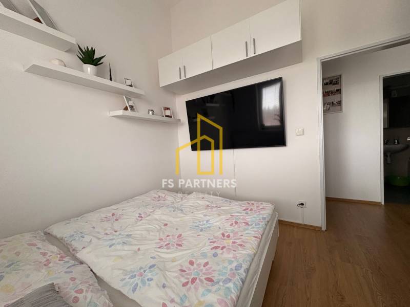 Világos hálószoba egy kétszobás lakásban, TV-vel és fa dekorációjú padlóval.