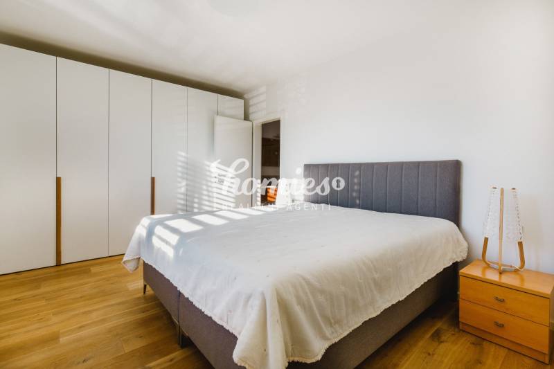 Hálószoba nagy ággyal, ruhásszekrénnyel és fa mintázatú padlóval egy családi házban.