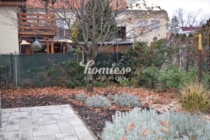 Családi ház kertje Nyitrán, fákkal, évelőkkel és burkolt felülettel.