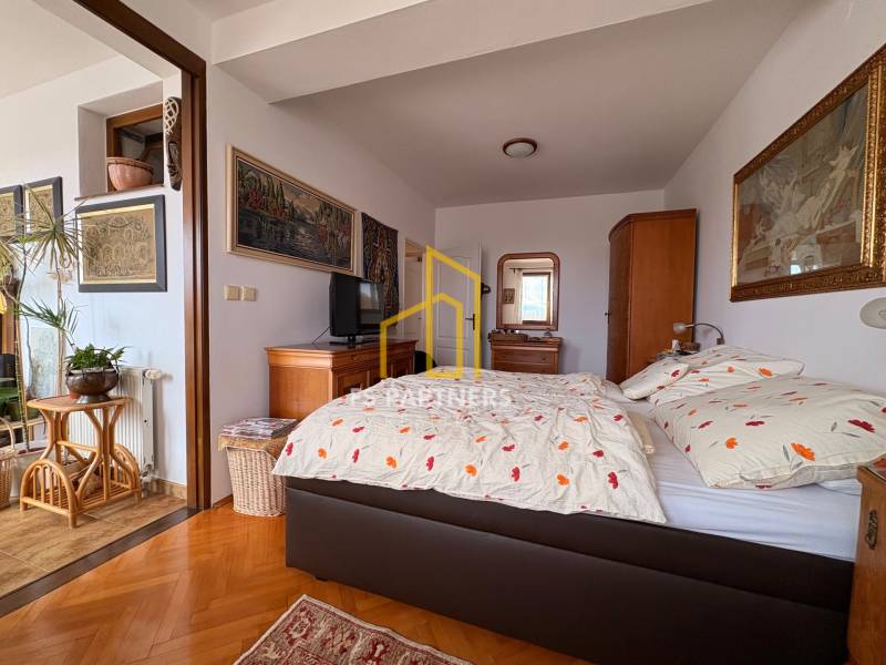 Öt vagy több szobás lakás szobája ággyal, művészettel a falakon és fa dekorációjú padlóval.