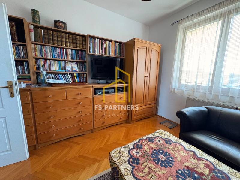 Szoba egy több szobás lakásban könyvtárral, televízióval és fa dekorációjú padlóval.