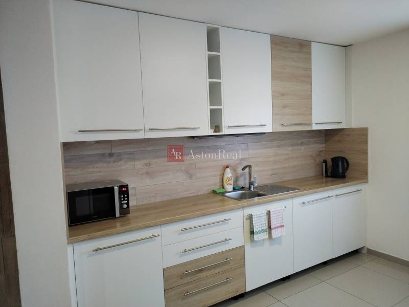 Konyha a házikóban fehér szekrényekkel és fa dekorációjú padlóval.