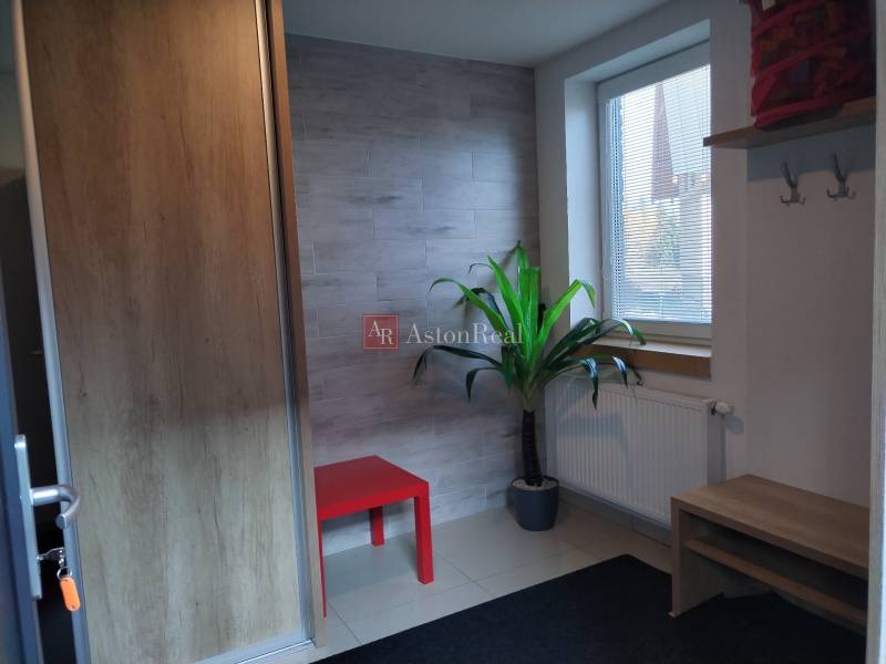 Egy kunyhó belseje piros asztallal, növénnyel, radiátorral és fa dekorációval ellátott fallal.