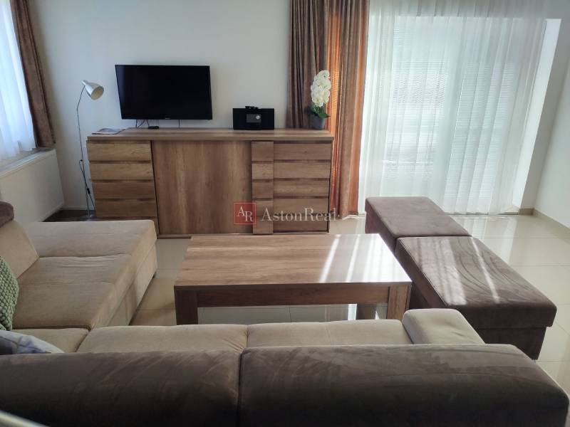 Nappali egy házikóban kanapéval, komódon lévő TV-vel és fa dekorációjú padlóval.