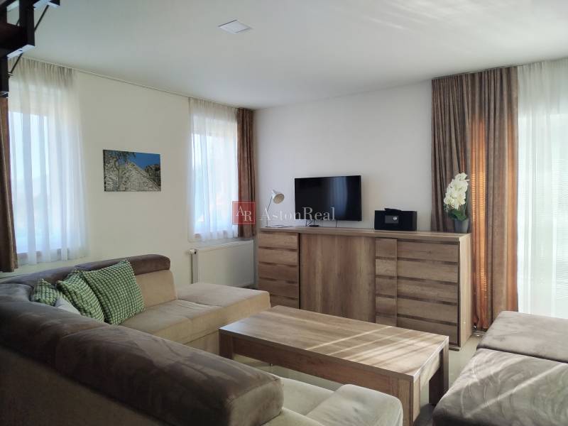 Világos szoba a házikóban kényelmes kanapéval és fa mintázatú padlóval.