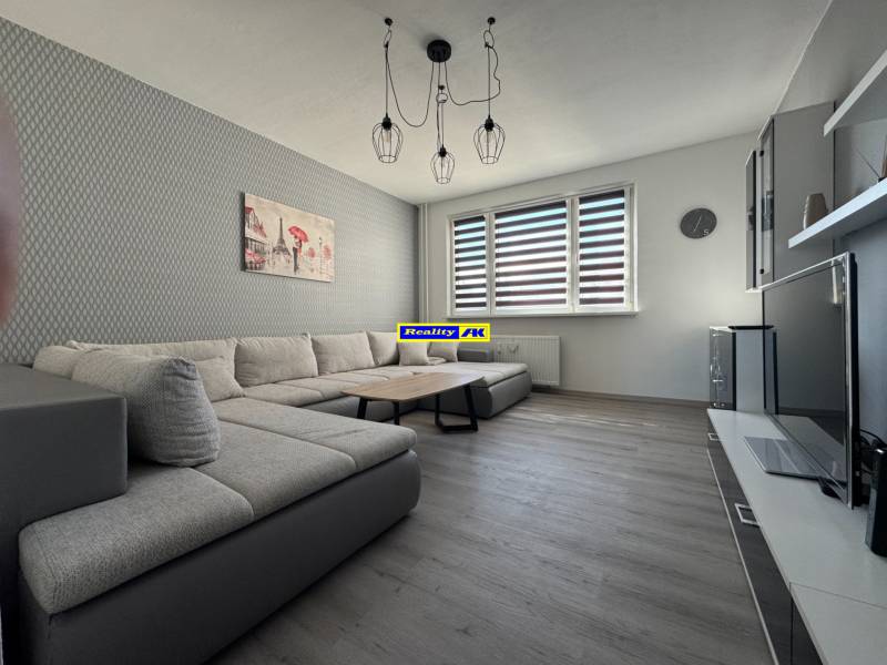 Nappali egy háromszobás lakásban kanapéval és fa dekorációjú padlóval.