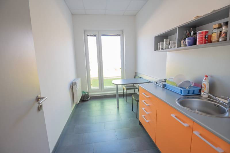 Irodai konyha narancssárga szekrényekkel, mosogatóval és ülőasztallal.