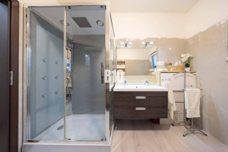 Családi ház fürdőszobája fa dekor padlóval, zuhanyzóval és tükörrel.