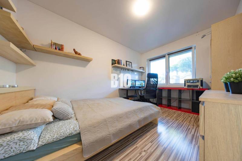 Hálószoba családi házban íróasztallal, polcokkal és fa dekorációjú padlóval.