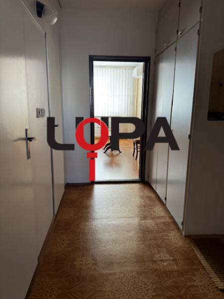 Háromszobás lakás folyosója fa dekor padlóval, amely világos helyiségbe vezet.