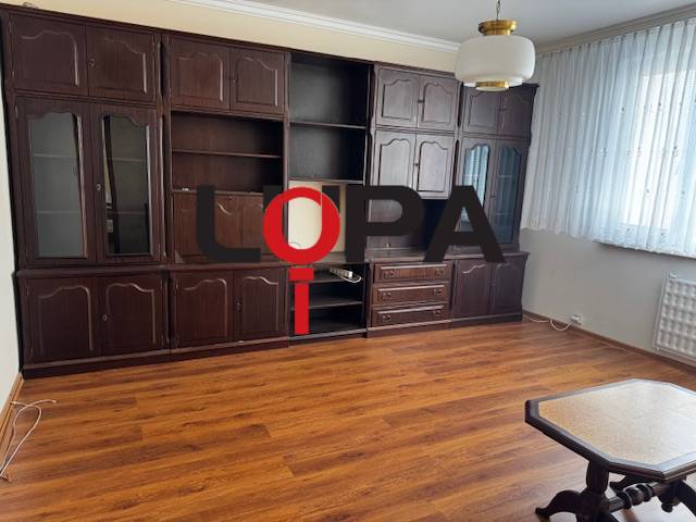 Nappali egy háromszobás lakásban, fa dekor padlóval, sötét bútorokkal.