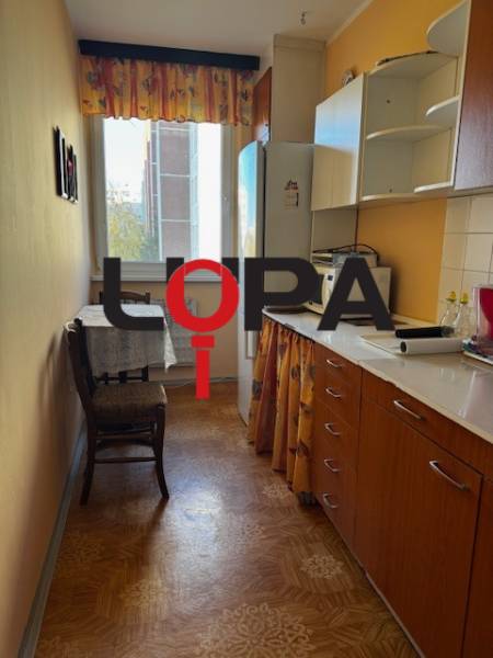 Konyha egy 3 szobás lakásban, fa dekor padlóval és meleg színű bútorokkal.