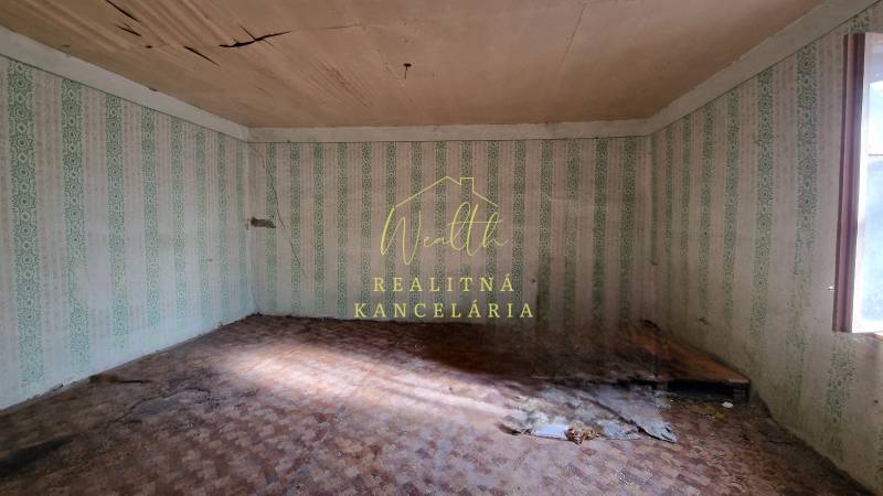 Szoba egy családi házban, sérült mennyezettel, tapétákkal és fa dekorációjú padlóval.