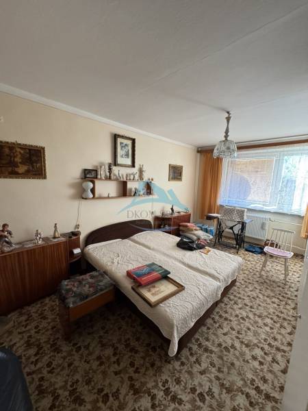 Szoba egy háromszobás lakásban kisággyal, szőnyeggel és bútorokkal, dekorációkkal a falakon.