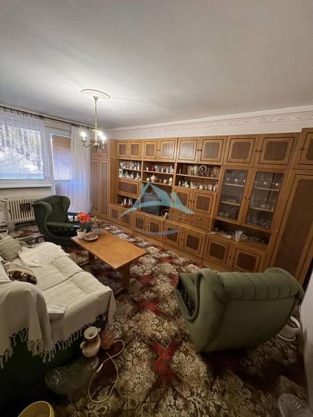 Nappali egy háromszobás lakásban, fa nappali szekrénnyel és zöld bútorokkal.