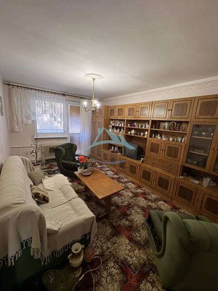 Nappali egy háromszobás lakásban, fa nappali fallal és kényelmes ülőgarnitúrával.