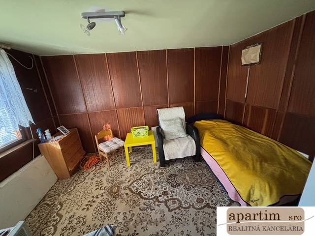 Szoba székekkel, ággyal, szekrénnyel és dekoratív szőnyeggel a Kertekben.