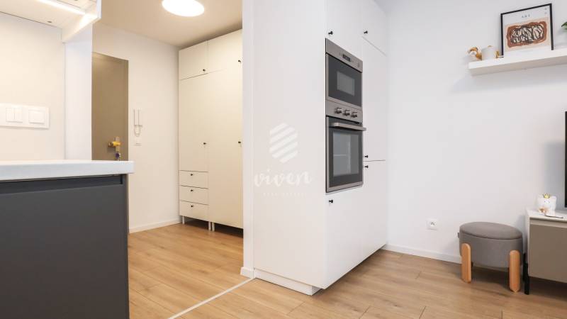 Konyha egy egyszobás lakásban fehér szekrényekkel és fa mintázatú padlóval.