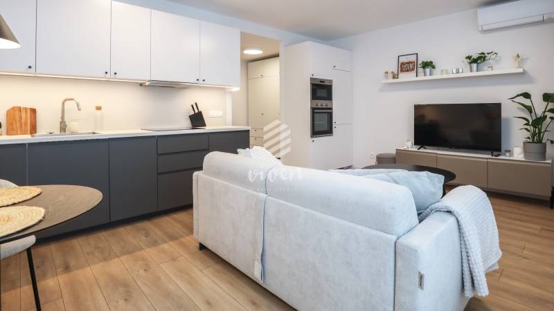 Nappali egy egyszobás lakásban konyhabútorral, kanapéval és fa dekor padlóval.