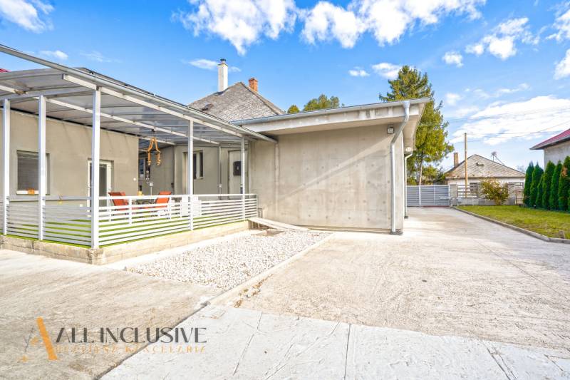 Családi ház Nagykosihán: beton terasz, előtető, kert, kék égbolt.