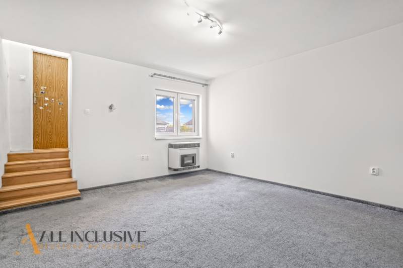 Fehér szoba szőnyegpadlóval, fa lépcsőkkel és ablakkal rendelkező fallal egy családi házban.