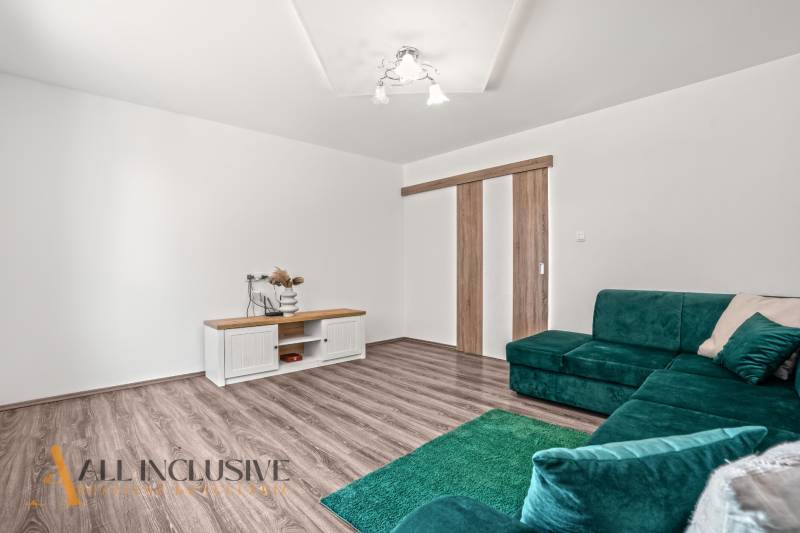 Családi ház belső tere fa dekoros padlóval, zöld kanapéval és asztallal.