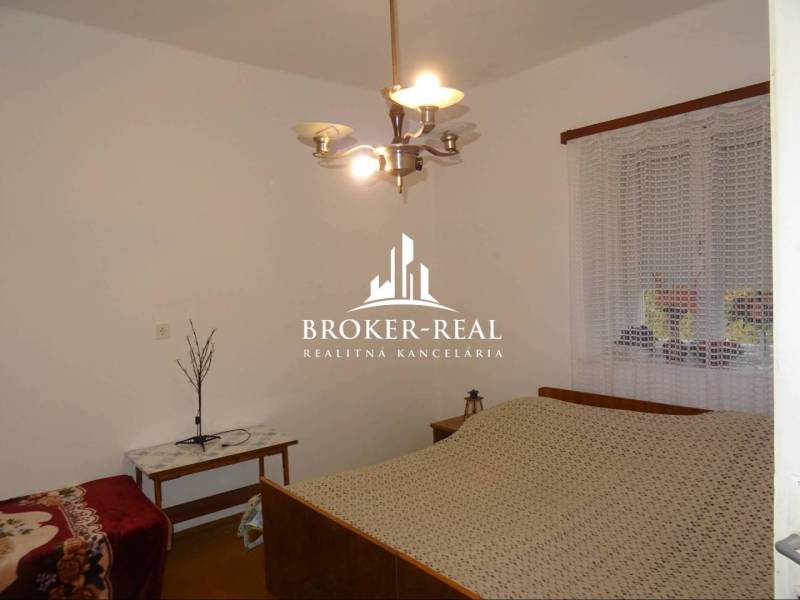 Hálószoba családi házban ággyal, asztallal és csillárral, a falon függönnyel ellátott ablak található.